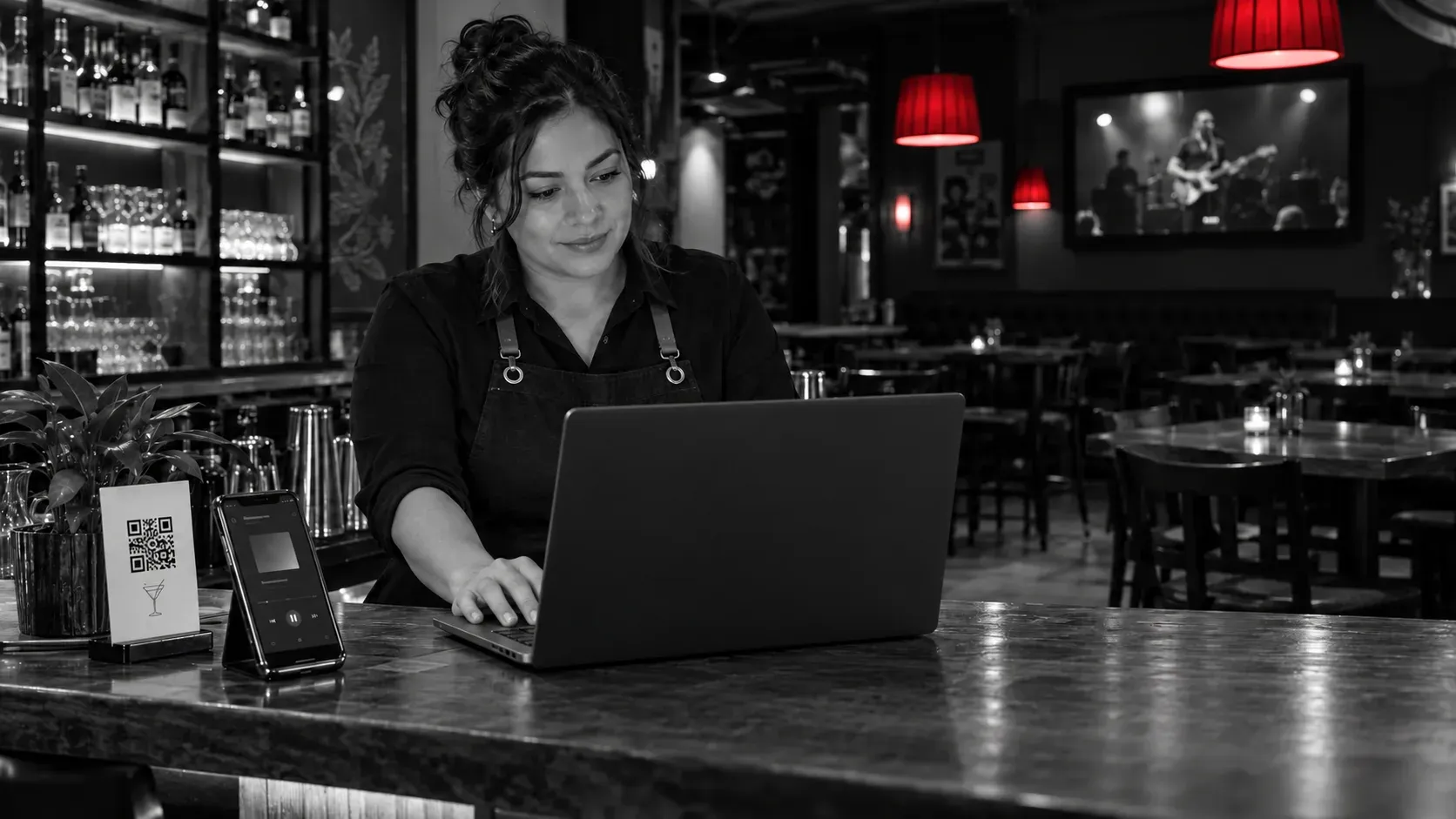 Administradora de un bar usando un portátil, con la tapa trasera hacia la cámara, junto a un QR
